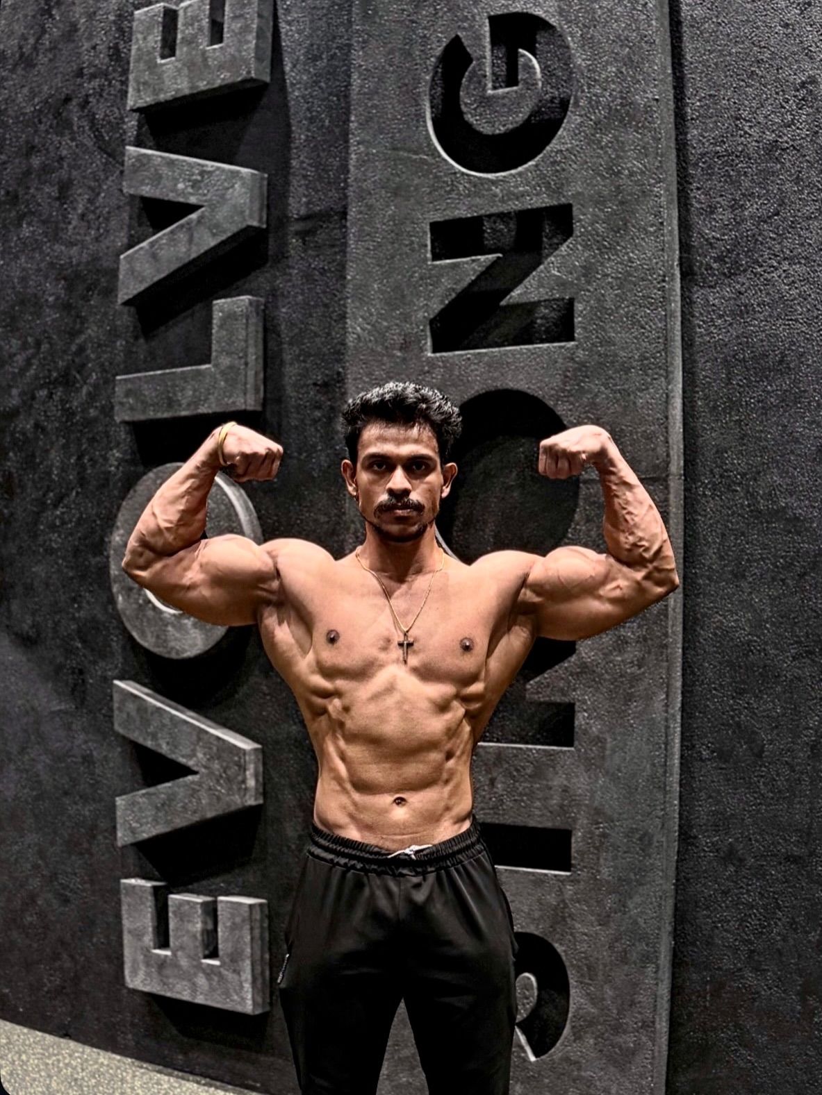 B6 athlete front double-bicep pose at the EVOLVE STRONG wall
